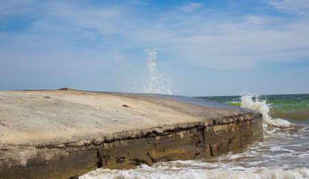 A long and empty tan pier stops the waves of the sea. A small storm. Free space for inscription.