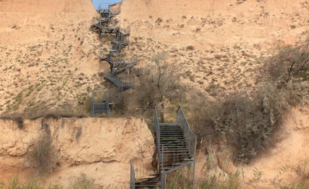 A steep metal staircase along a vertical yellow-brown clay slope, a small piece of blue sky at the...