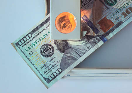 Checking money for authenticity. Benjamin Franklin on the 100 dollar bill looks into the frame through a magnifying glass of a special device. Portrait of Benjamin Franklin under examination.の写真素材