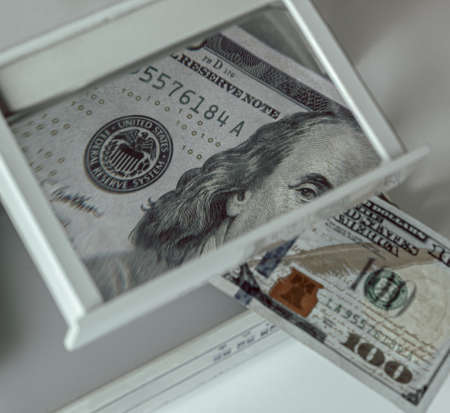 Checking money for authenticity. Benjamin Franklin on the 100 dollar bill looks into the frame through a magnifying glass of a special device. Checking dollarsの写真素材