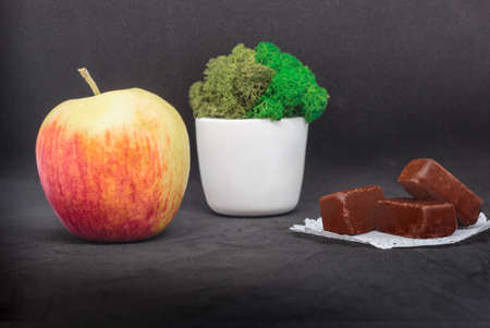 A large juicy peach separates a white pot of moss from the chocolates. The concept of natural and...