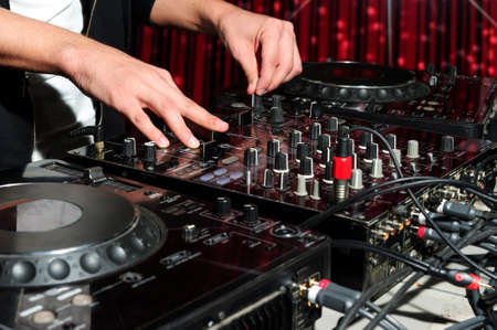 DJ at dance party mixes track on sound mixer, nightclub with striped red interior, professional stereo electronic equipmentの写真素材