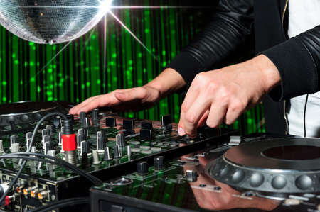 DJ at dance party mixes track on sound mixer, nightclub with striped green interior and silver disco ball with star, professional stereo electronic equipmentの写真素材
