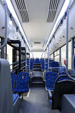 Bus inside, city transportation white interior with blue seats in row, retirement places, open doors, handles for standing passengers, bright lights and air conditionerの写真素材