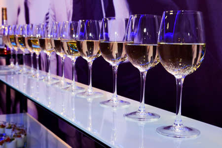 Nightclub wine glasses with white wine lit by party festive lights on dark-purple background, nightlifeの写真素材