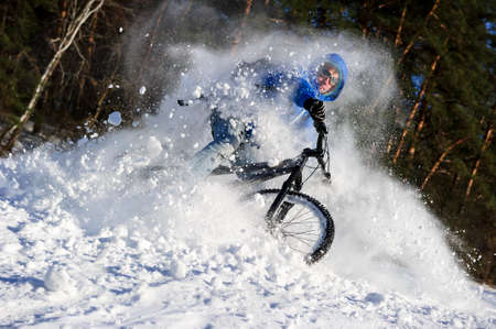 Extreme cyclist riding mountain bike in flying snow near winter forest in sunny cold dayの写真素材