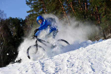 Cyclist on mountain bicycle, extreme cycling in flying snow near winter forest, sunny cold dayの写真素材