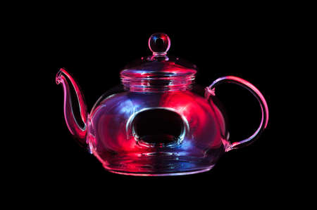 Glass tea kettle lit by red, blue, lilac lights, empty teapot isolated on black background, studio...