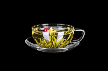 Green tea with red flower in transparent glass cup on saucer, studio shot, isolated on black