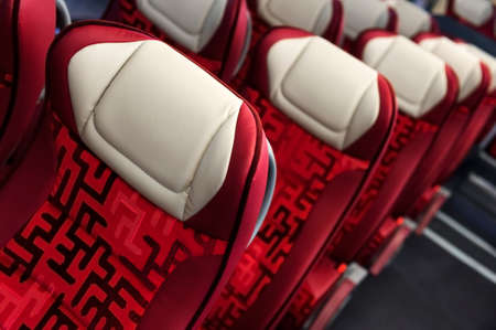 Bus seats in row with red leather, textile coating, wooden armrests, white headrests and mounts for safety belts, modern comfortable tourist transport interior, selective focusの写真素材