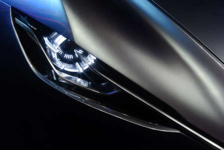 Predatory car headlight and hood of powerful sports grey car with blue glare on dark background