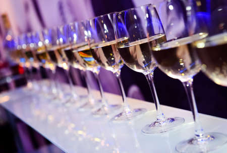 Nightclub wine glasses with white wine lit by party festive lights on dark-purple background, nightlife entertainment industryの写真素材