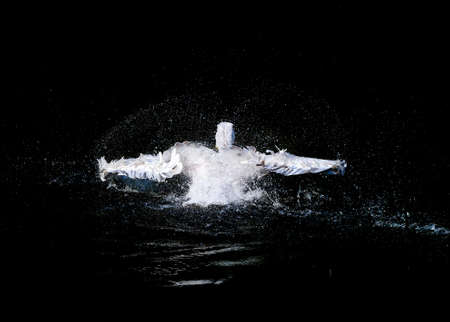 Big white pelican with flapping wings and blue drops swimming in black water of dark ocean, wildlifeの写真素材