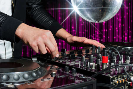 DJ at nightclub party playing on sound mixer, striped pink interior and silver disco ball with star on background, nightlife entertainment industryの写真素材