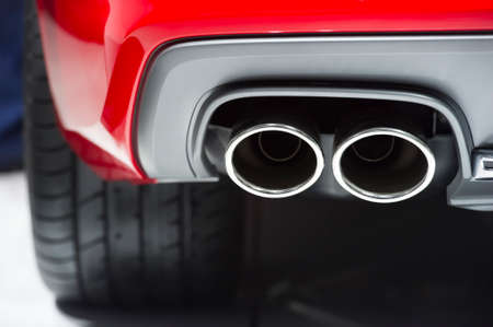 Chrome exhaust pipes of powerful sport car with red bodywork and grey bumperの写真素材