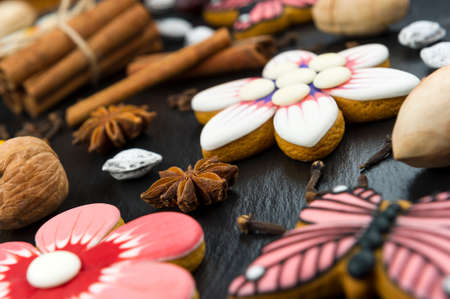 Gingerbread cookies with nuts and spices, colorful homemade cakes in shape of flower and erfly on black textured background, selective focusの写真素材