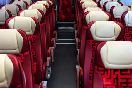 Bus seats in row with red leather, textile coating, wooden armrests, white headrests and mounts for safety belts, modern comfortable tourist transport interior, selective focusの写真素材