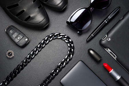 Woman accessories in business style, red lipstick, gadgets, jewelry, car key, sunglasses, shoes, and other luxury businesswooman attributes on leather black background, fashion industry, selective focusの写真素材