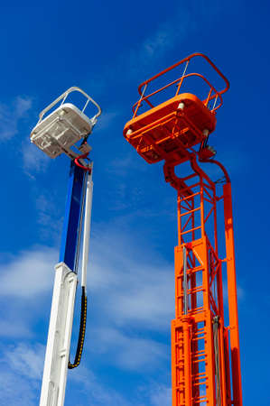 Lift platform with bucket and cherry picker aerial work platforms, construction hydraulic telescopic cranes of orange and white colors, heavy industry, blue sky on backgroundの写真素材