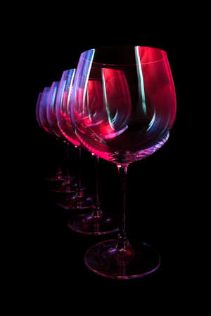 Party wine glasses in nightclub lit by red, blue, lilac lights, nightlife and entertainment industry, objects in row isolated on black backgroundの写真素材
