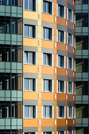 Windows of apartment blocks, residential building in modern architectural style, custom curved orange wall with white and gray construction tile and glazed balconies in green and turquoise shadesの写真素材