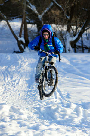 Cyclist on mountain bicycle, extreme jumping in snow field near winter forest, sunny cold eveningの写真素材