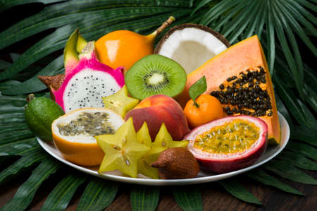 Exotic tropical fruits dish on palm leaves and wooden background, healthy food, diet nutrition, selective focusの写真素材