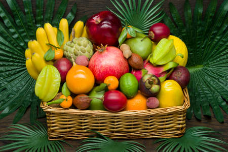 Fresh Thai fruits in wicker basket on palm leaves and wooden background, healthy food, diet nutritionの写真素材