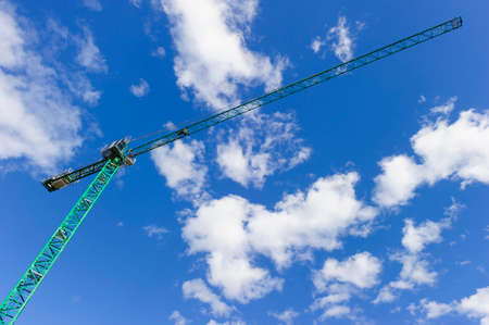 Green construction tower crane, heavy industry, blue sky and white clouds on background, bottom viewの写真素材