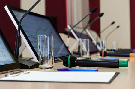 Conference room table for business meeting with microphones, monitors, pens, papers, glasses for water in row, selective focusの写真素材