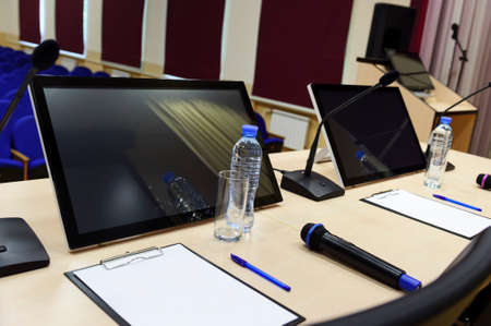 Conference room for business meeting, table with microphones, monitors, bottles with water, glasses,...