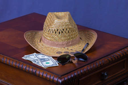 Hat, sunglasses, pen and money on wooden deskの写真素材
