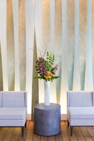 Floral arangement with Cymbidium and James Storey orchids, Hydrangea, Curly willow, Yellow pin cushion protea and greenery in white cylinder vase, and two beige chairsの写真素材