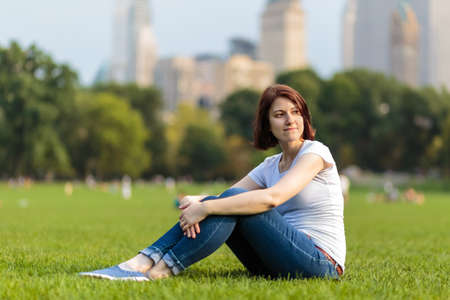 Relaxing beautiful girl sitting on green grass. Summer meadow.の写真素材
