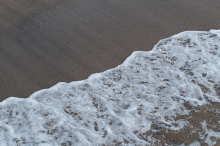 Close-up view of textured white ocean foam meeting dark brown sandの写真素材