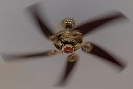 Classic brass ceiling fan with dark wooden blades spinning rapidly overheadの写真素材