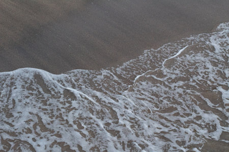 Close-up view of textured white ocean foam meeting dark brown sand