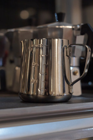 Close-up of shiny stainless steel milk frothing pitcher with measurement markings for baristaの写真素材