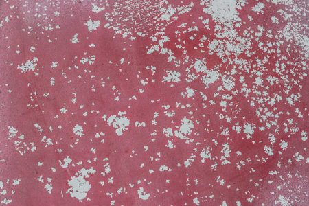 Close up of aged surface showing distressed pinkish red paint with white flakes