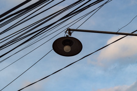 Cluttered Power Lines and Old Street Lamp Against Cloudy Sky in Urban Areaの写真素材
