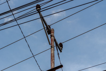 Overhead electrical power lines and communication cables attached to a rusty utility pole against blue sky.の写真素材