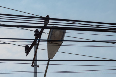 Complex network of overhead electrical wires and a street lamp against the sky.の写真素材