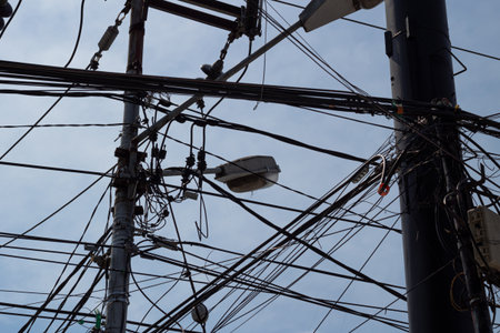 Tangled cluster of power lines and utility cables creating chaos against a blue sky.