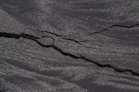 Black Volcanic Sand Texture with Horizontal Wavy Layers and Diagonal Earthquake Crack Pattern Background.の写真素材