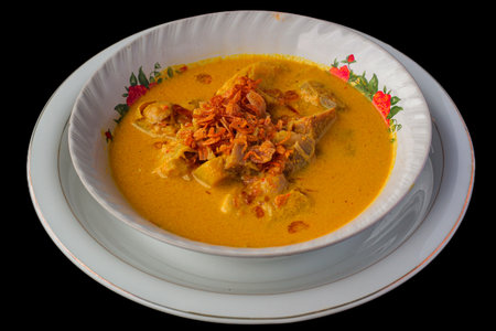 Traditional Indonesian Yellow Curry or Gulai Daging from Lombok served in a bowl with fried shallots on black background.の写真素材
