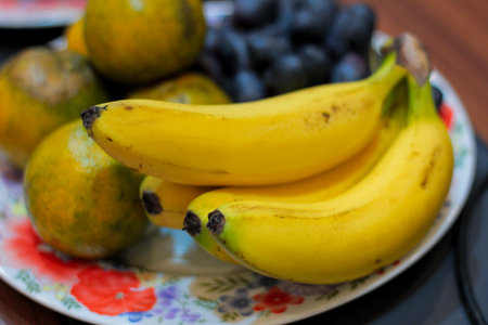 Vibrant cluster of yellow bananas centered on a decorated ceramic plate, complemented by defocused citrus and grapes.の写真素材