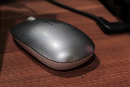Wireless computer mouse resting on a wood desk surface for office equipment and modern technology...