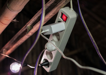 Overloaded electric extension cord with multiple plugs and a red power switch in a makeshift, dark...