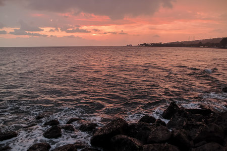 Sunset Over Ocean Waves Crashing on Rocks with Orange Sky and Space, conveying tranquility and...