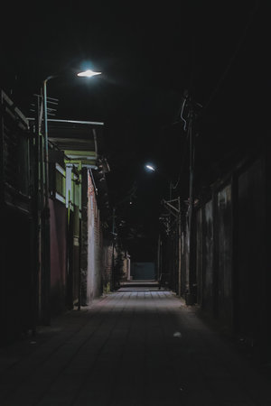 Dimly lit alleyway at night with streetlights creating a mysterious atmosphere and copy space, ideal...